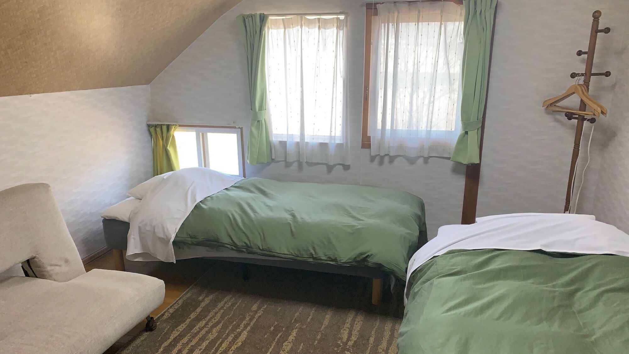 Een slaapkamer met twee bedden, een stoel, een houten bedframe en een raam met gordijnen.