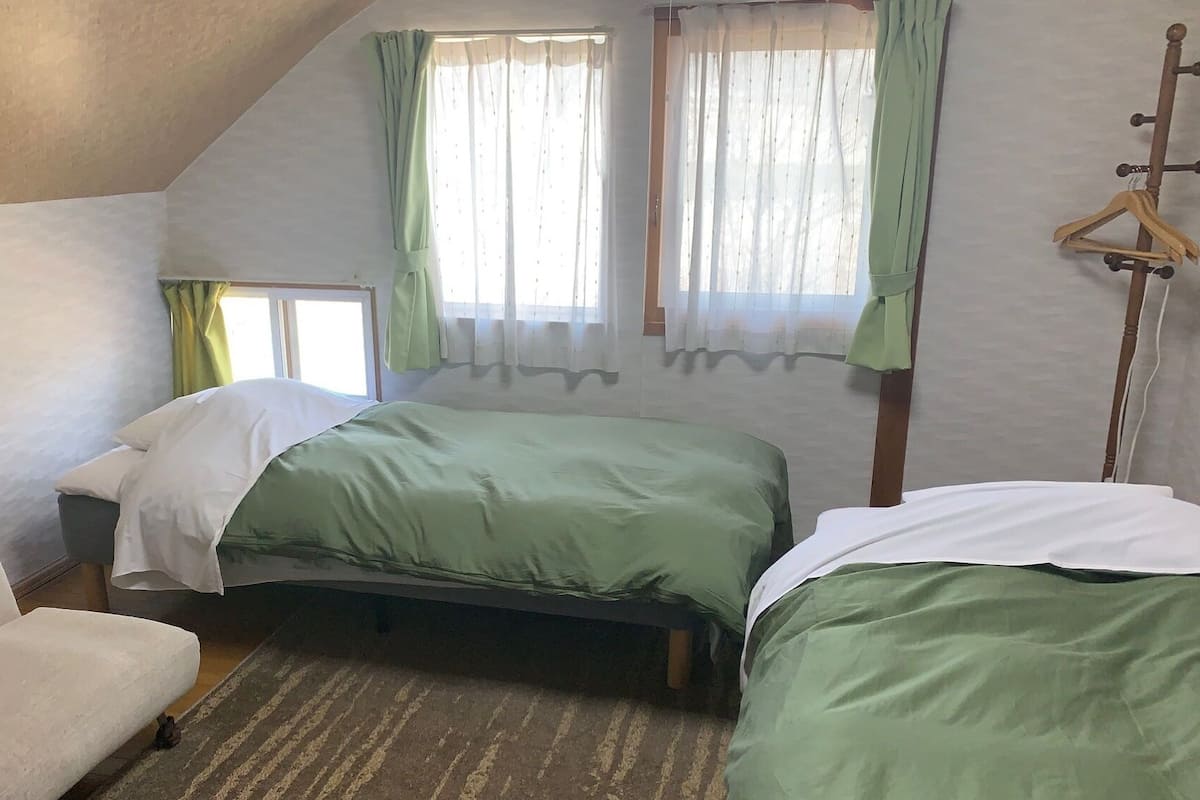 Una camera da letto con due letti, una sedia, una struttura letto in legno e una finestra con tende.