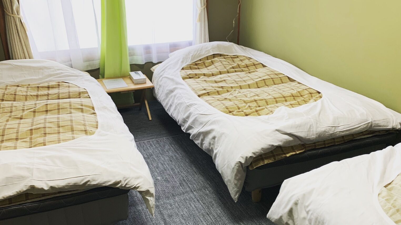 Een kamer met twee eenpersoonsbedden, een klein tafeltje en een raam met gordijnen.