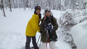 Two people in winter clothing standing in a snowy forest.