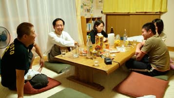 A group of people seated around a wooden table in a room with tatami mats, a fan, and various items on the table.