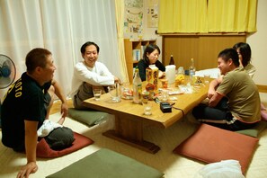 Un gruppo di persone seduto attorno a un tavolo di legno in una stanza con tatami, un ventaglio e diversi oggetti sul tavolo.