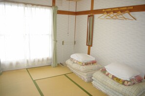 Una camera in stile tradizionale giapponese, con pavimento in tatami, schermo scorrevole shoji e un letto di legno con attaccapanni.