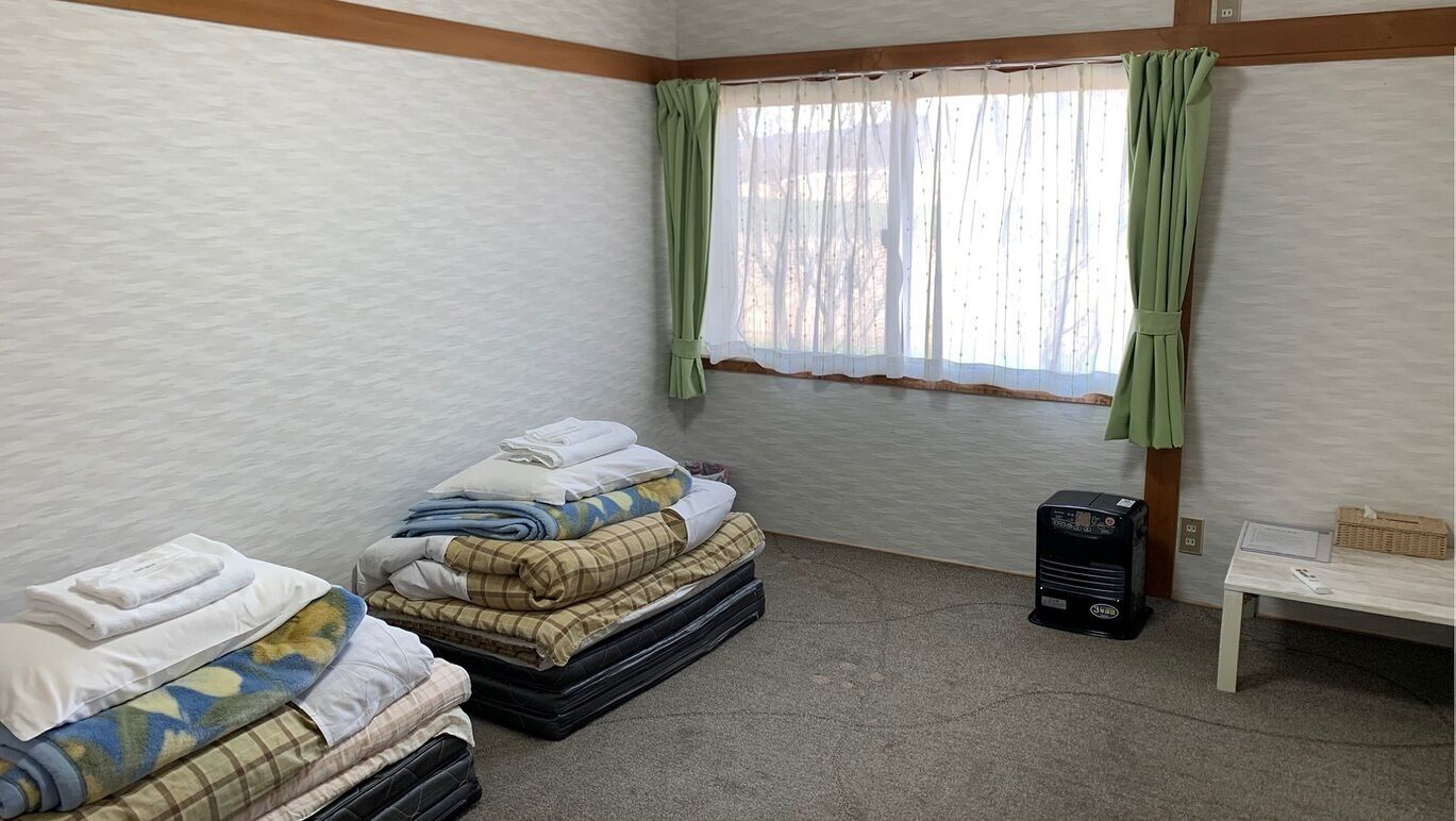 Una habitación con dos camas, una mesa, un calentador y una ventana con cortinas.