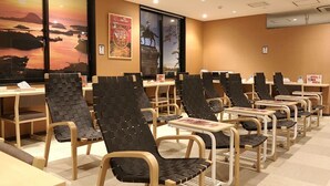 A hotel room with multiple tables and chairs, a large window with a view, and a poster on the wall. - Capsule Hotel Topos Sendai Station Nishiguchi (Sendai)