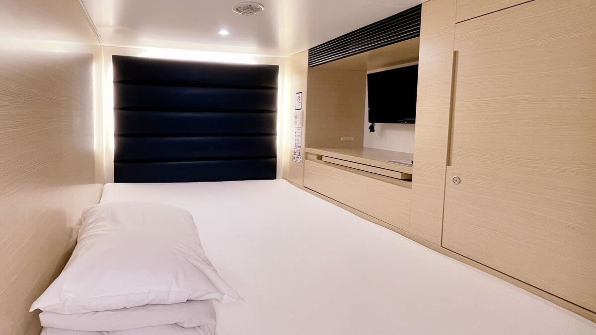 Un dormitorio con cama, armario, espejo y televisor en la pared.