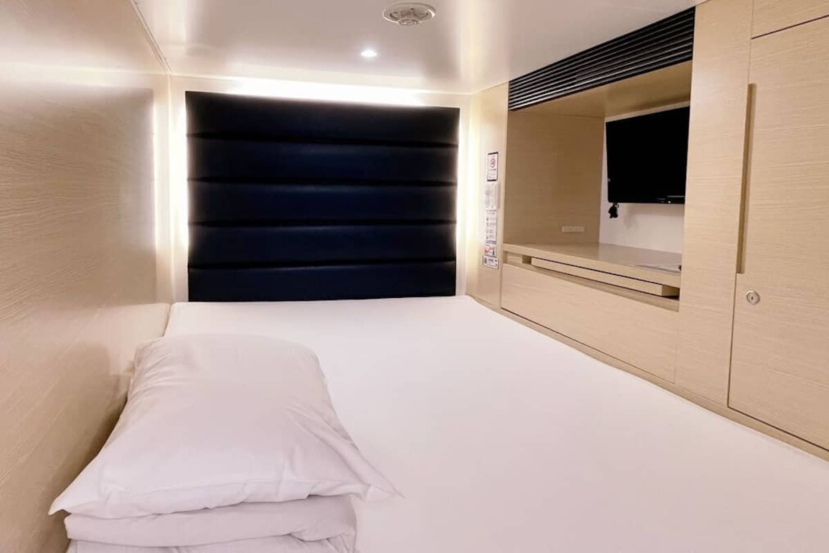 A bedroom with a bed, a wardrobe, a mirror, and a wall-mounted TV.