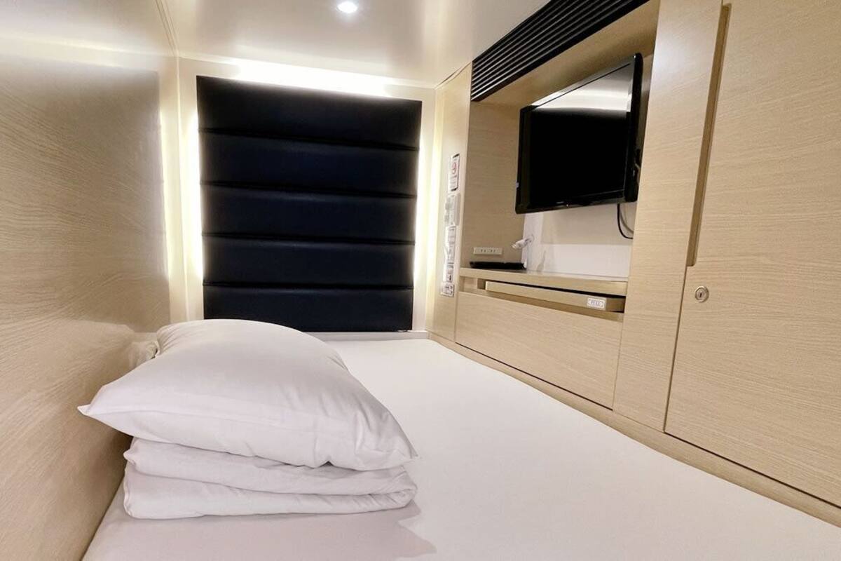 A compact room with a bed, a flat-screen TV mounted on the wall, and a wooden cabinet.