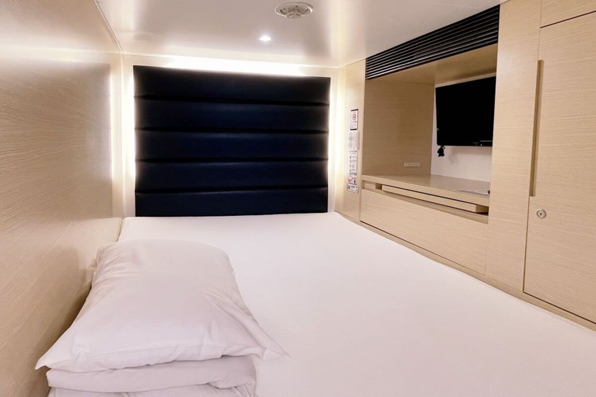 A bedroom with a bed, a wardrobe, a mirror, and a wall-mounted TV.