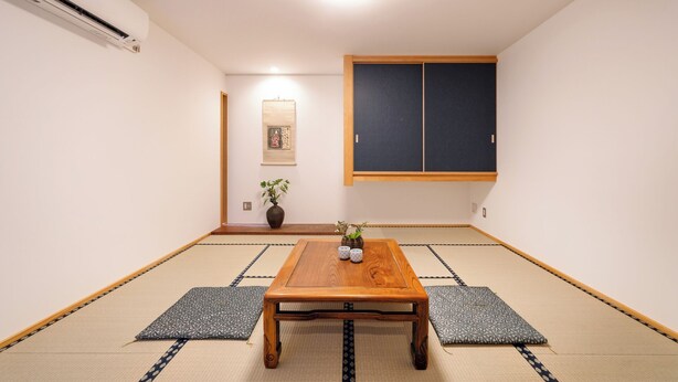 A traditional Japanese room with tatami flooring, a wooden table, a low wooden cabinet, and a wall-mounted air conditioner. - Chiisana Kinoie (Tokyo)