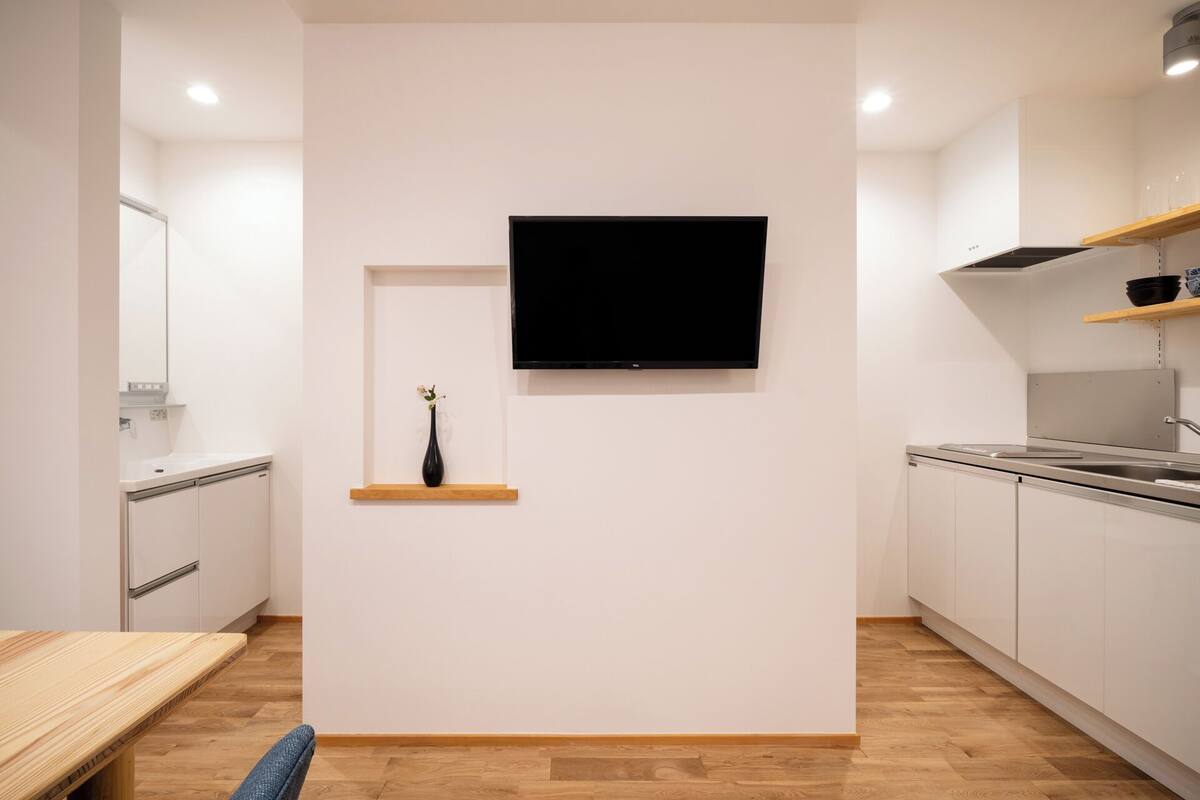A modern kitchen with white cabinetry, a wooden countertop, a black vase on a shelf, and a mounted flat-screen TV.
