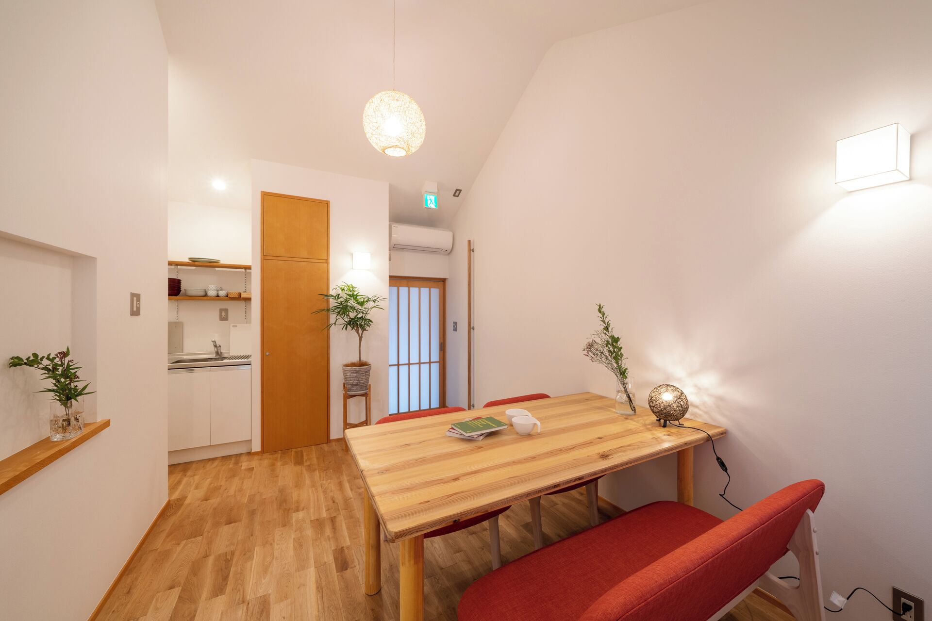 A dining area with a wooden table, red chairs, a potted plant, and a hanging light fixture.