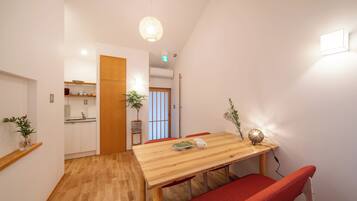 A dining area with a wooden table, red chairs, a potted plant, and a hanging light fixture.