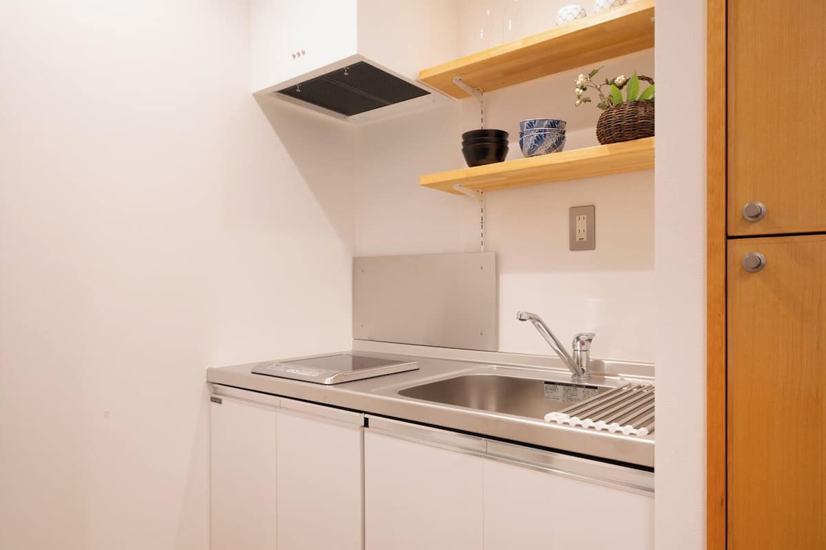 A compact kitchen with white cabinets, a stainless steel sink, a built-in oven, and wooden shelves above the counter.