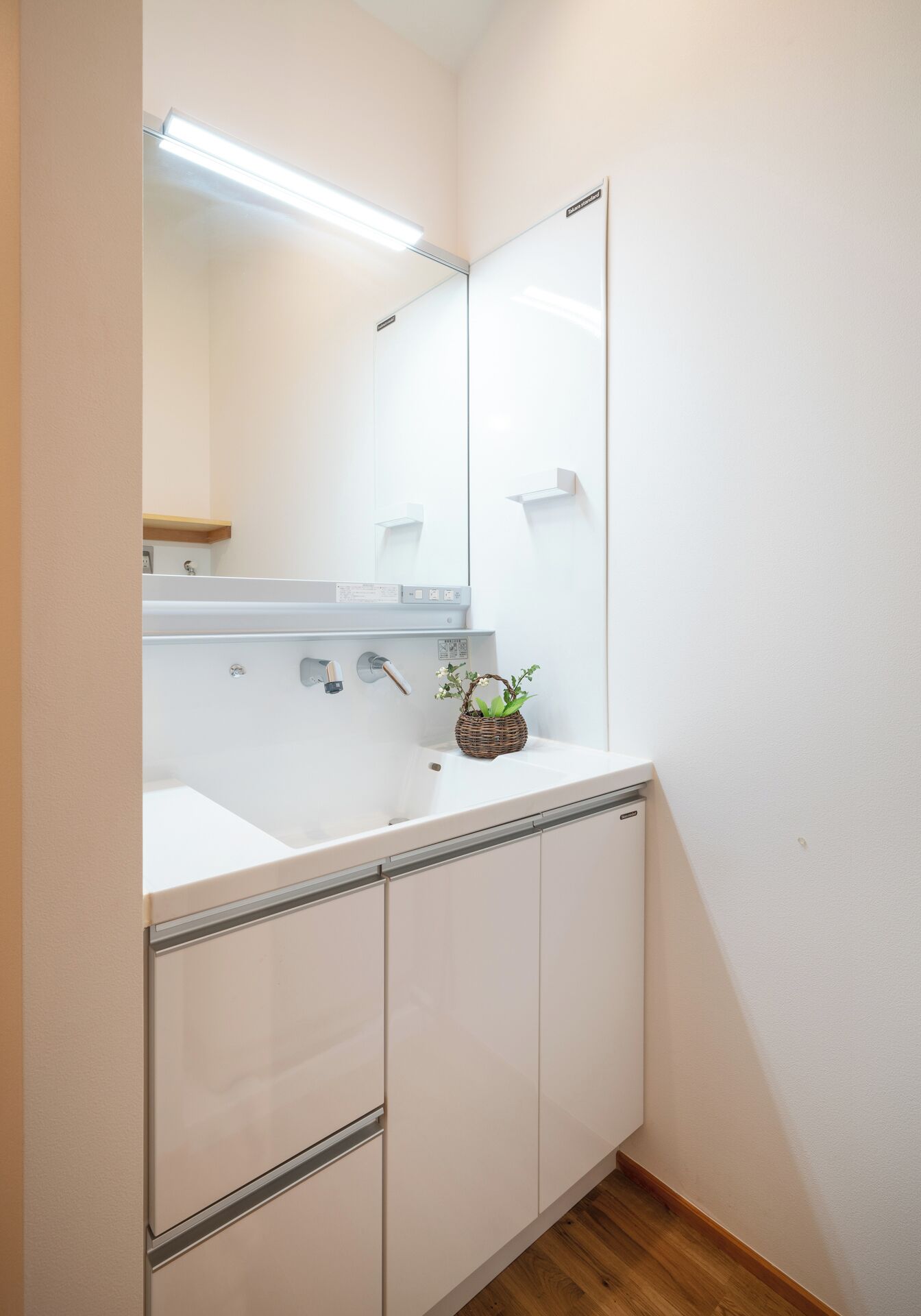 A bathroom with a white sink, mirror, and wooden floor.