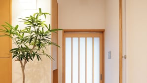 A hallway with a wooden floor, a potted plant, a sliding door, and a light fixture on the ceiling. - Chiisana Kinoie (Tokyo)
