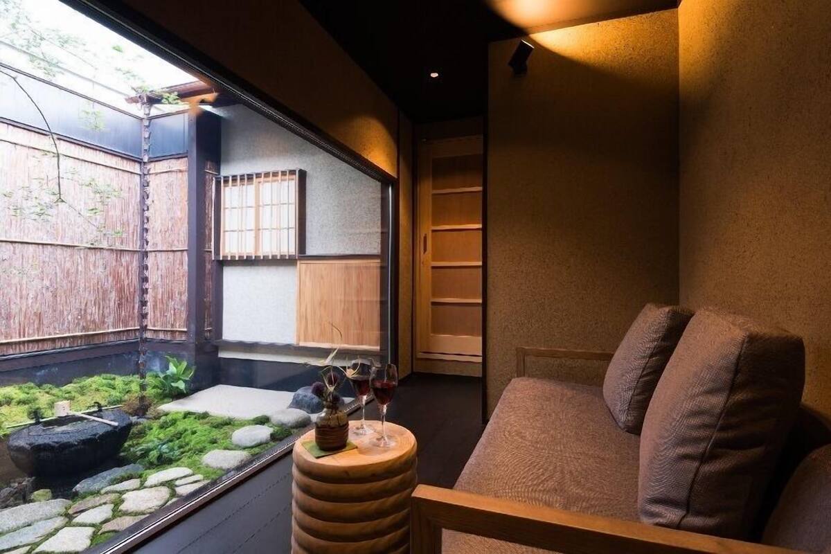 Ein Zimmer mit Gartenblick, eine Holzbank, eine Couch und ein kleiner Tisch mit einer Flasche und Gläsern.