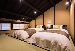 A traditional Japanese-style room with tatami flooring, two beds with white and brown bedding, a low ceiling with wooden beams, and a wall with shoji screens. - Kyomachiya Stay Takasegawa Shichijo (Kyoto)