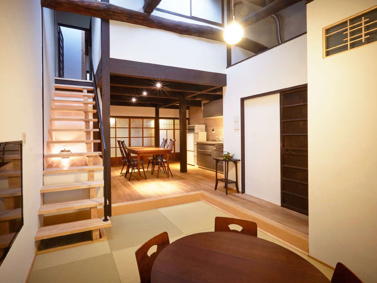Um interior moderno com escada, área de refeições, cozinha e uma janela grande.