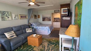 A living room with a sofa, a small table, a bed, a kitchenette, and a ceiling fan. - Cozy studio with refreshing AC, pool, and 3-minute walk to the beach (Atlantic Beach)