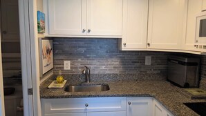 A kitchen with white cabinets, a granite countertop, a stainless steel sink, and a microwave. - Cozy studio with refreshing AC, pool, and 3-minute walk to the beach (Atlantic Beach)