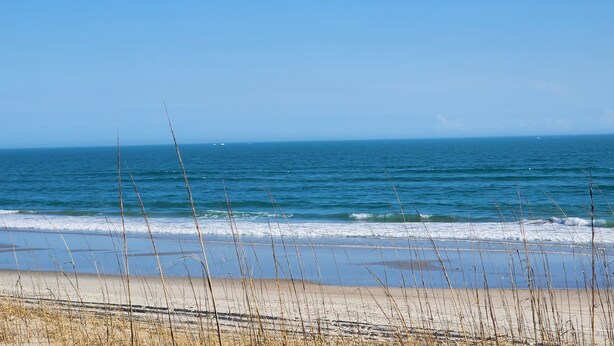 A beach with waves, a clear sky, and distant boats. - Cozy studio with refreshing AC, pool, and 3-minute walk to the beach (Atlantic Beach)
