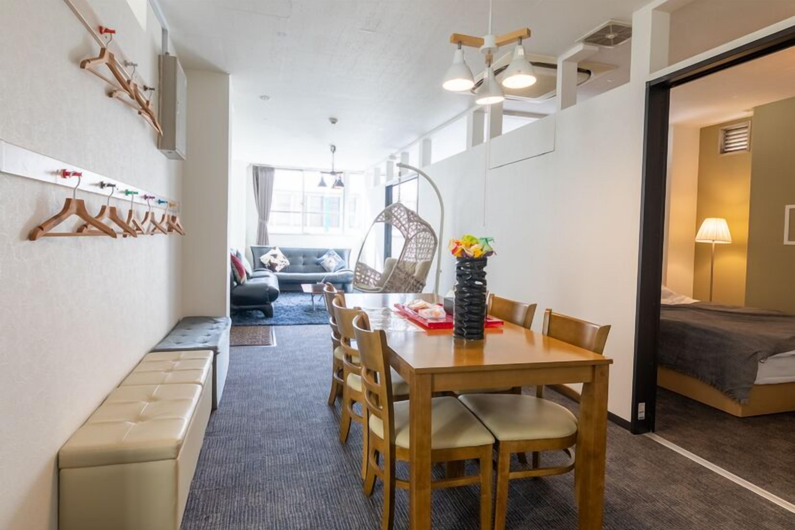 A compact room with a dining table, chairs, a bench, a bed, a hanging chair, and a wall-mounted coat rack.