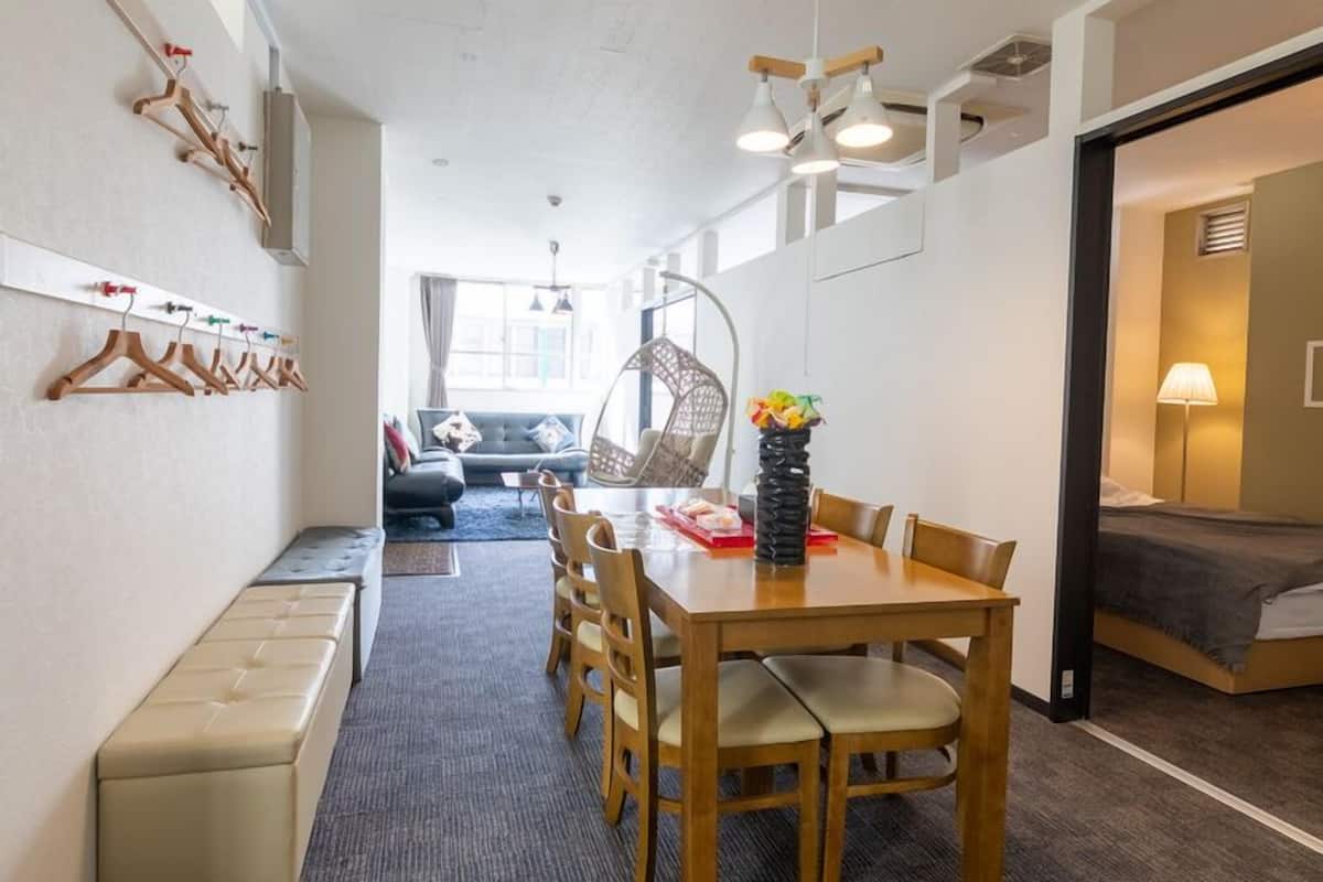 A compact room with a dining table, chairs, a bench, a bed, a hanging chair, and a wall-mounted coat rack.