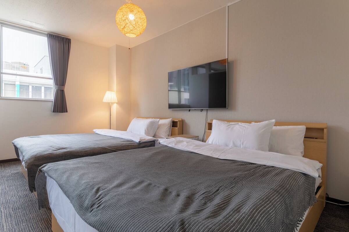 A hotel room with two beds, a TV, a lamp, and a window with curtains.