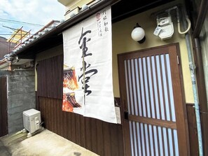 En traditionel japansk bygning med et stort banner, træskydedøre og en lille airconditionenhed.