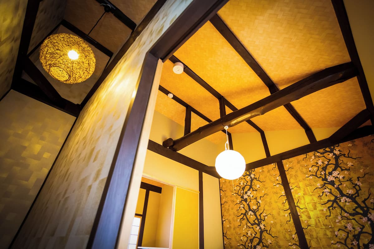 Una habitación con vigas de madera a la vista, pared con textura y un diseño de árbol, y lámparas colgantes esféricas.
