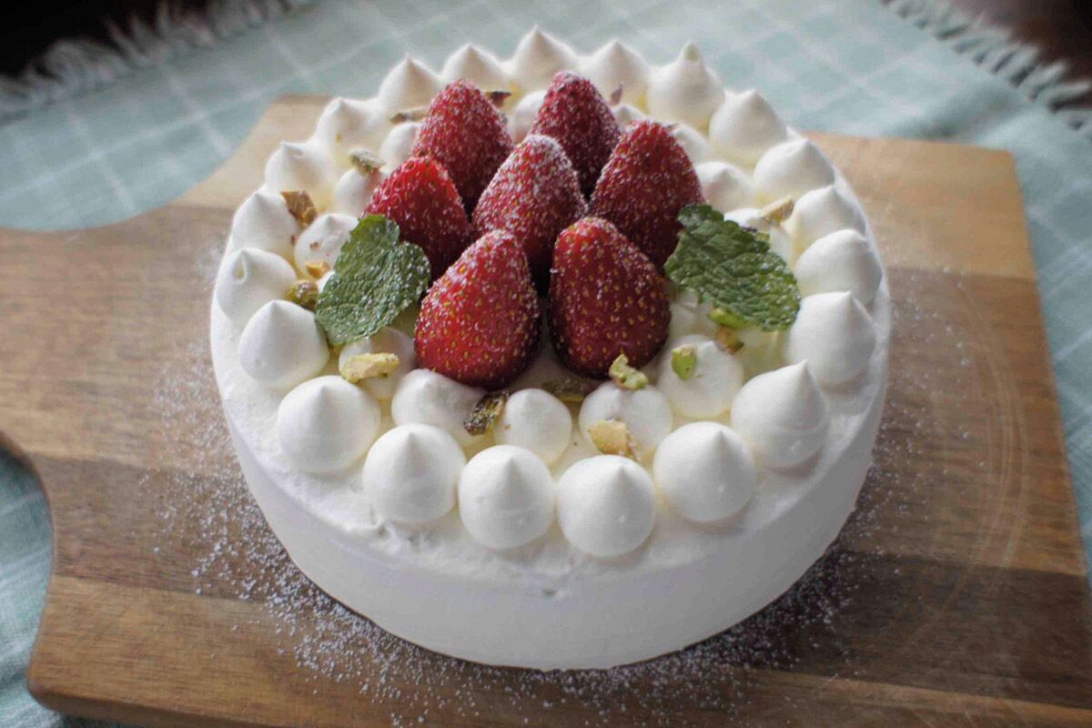 A round dessert with strawberries and mint leaves on a wooden board.