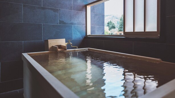 Un jacuzzi rectangular con estructura de madera, un taburete de madera y una ventana con paneles de vidrio esmerilado.