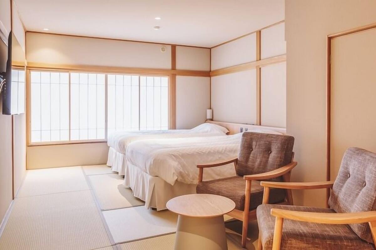 Una habitación de hotel con cama, dos sillas, una mesita y televisor.
