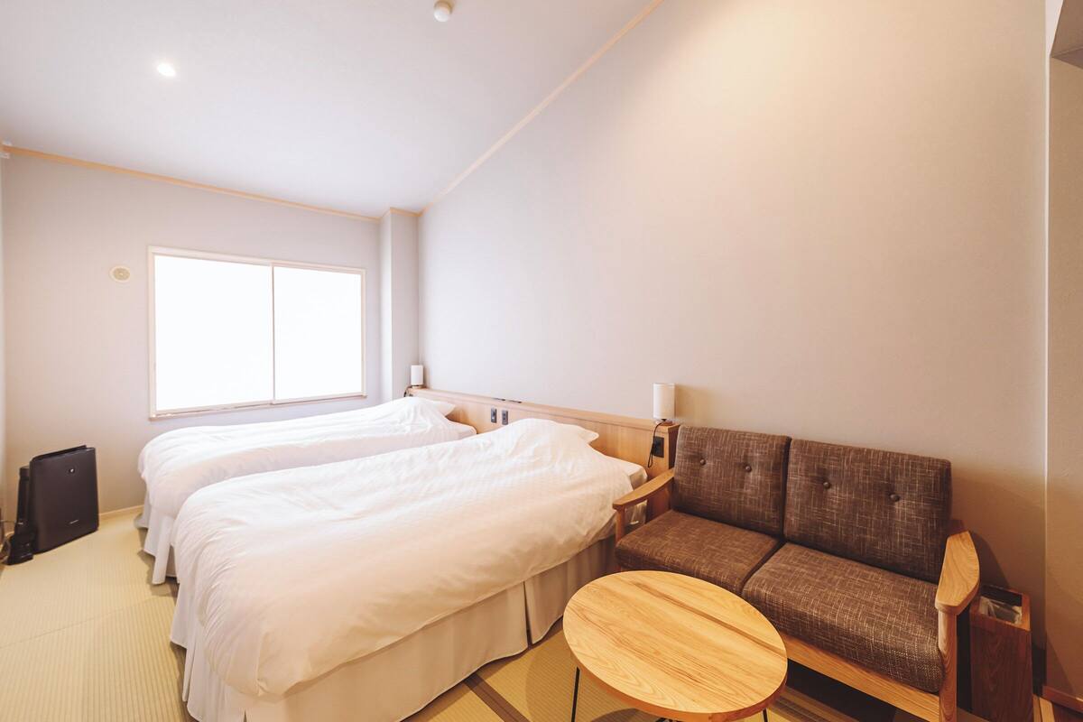 Una habitación de hotel con dos camas, un sofá, una pequeña mesa de madera y una ventana.