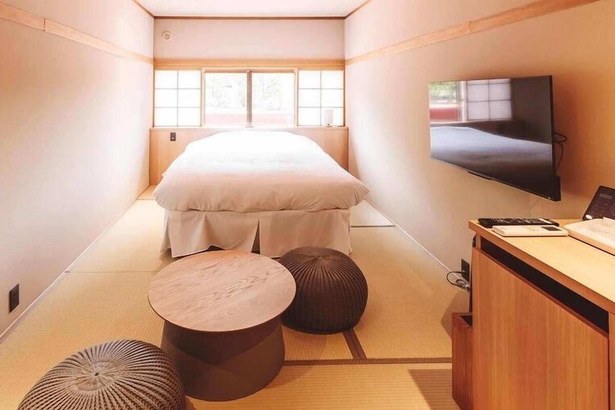 Una habitación con suelo de tatami, una cama, un televisor y un escritorio con una silla.