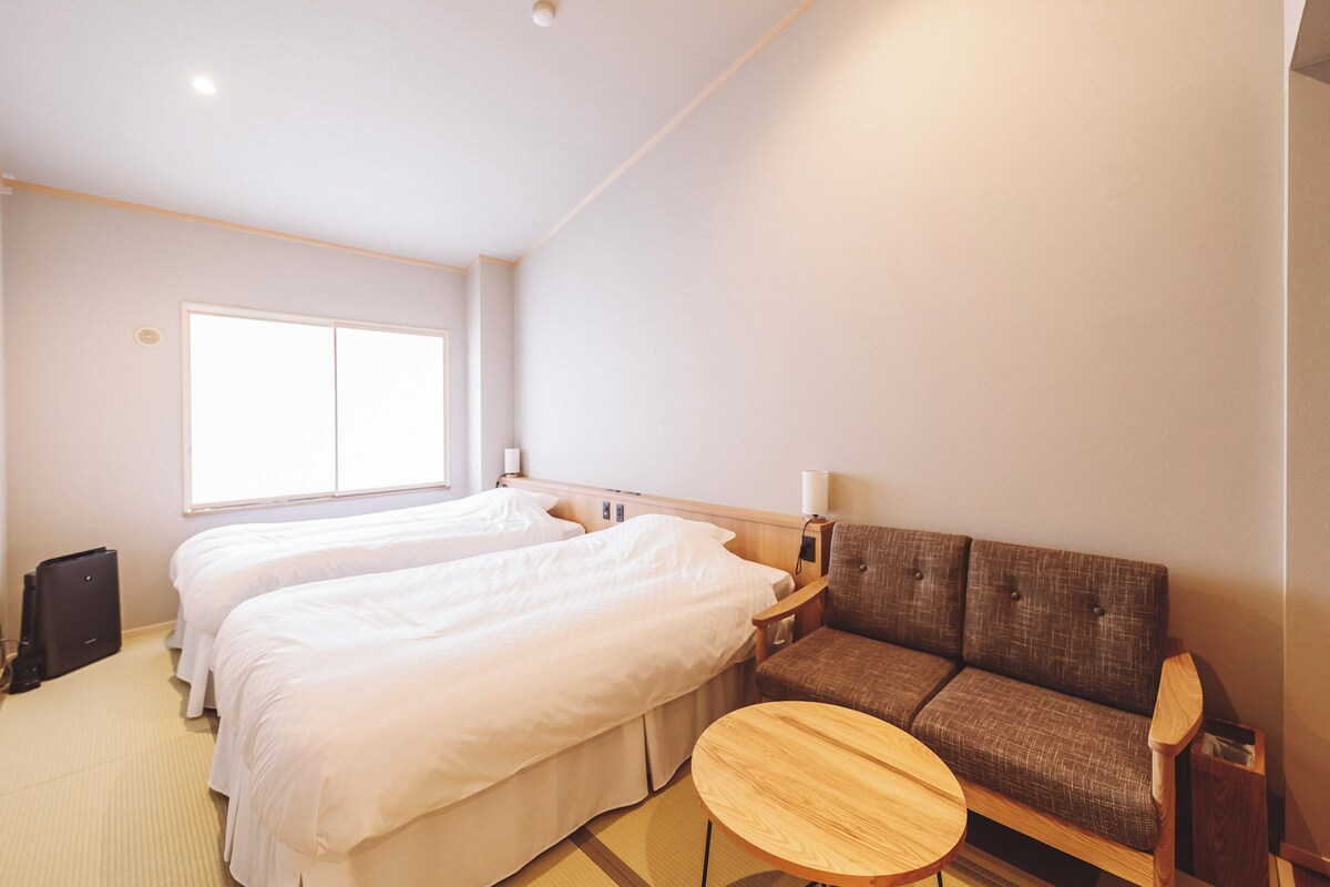 A hotel room with two beds, a sofa, a small wooden table, and a window.