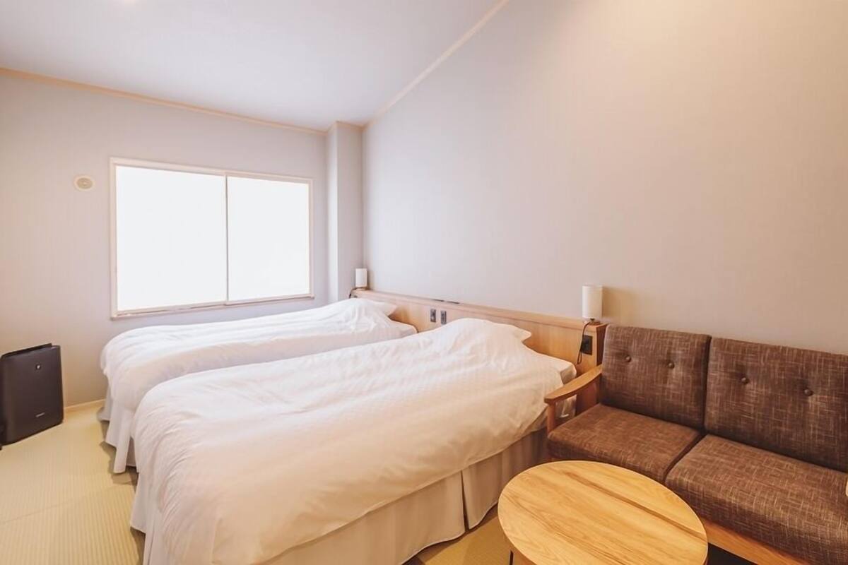 Una habitación de hotel con dos camas, un sofá, una mesita y un ventanal.