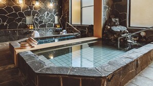 Un espacio de spa con paredes de piedra, un hidromasaje, un banco de madera y un borde de piedra.