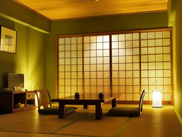 A traditional Japanese room with tatami flooring, a low table with a tea set, a sliding door, and a desk with a computer.