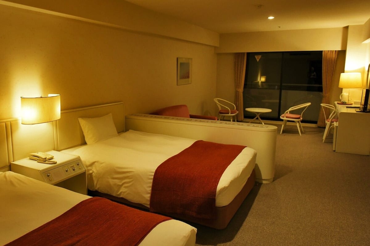 A hotel room with two beds, a desk, a chair, and a small table.