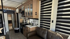 A compact RV interior with a kitchenette, a seating area, and a sliding door. - Modern Luxury RV Retreat and Patio, minutes from springs and beaches! (DeFuniak Springs)
