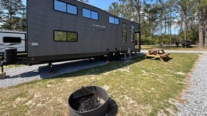 A mobile home with a kitchen area, a dining table, and a grill. - Modern Luxury RV Retreat and Patio, minutes from springs and beaches! (DeFuniak Springs)