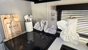 A kitchenette with a wooden cutting board, a container of utensils, a paper towel holder, and a window with blinds. - Modern Luxury RV Retreat and Patio, minutes from springs and beaches! (DeFuniak Springs)