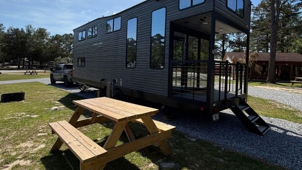 A modern, two-story mobile home with a covered porch and a picnic table in front. - Modern Luxury RV Retreat and Patio, minutes from springs and beaches! (DeFuniak Springs)