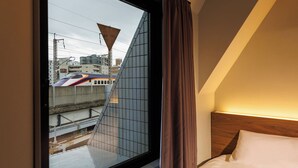 A hotel room with a large window, a bed, and a view of a train passing by. - Hotel B4T Akabane (Tokyo)