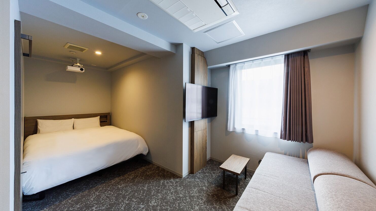 A hotel room with a bed, a sofa, a TV, a projector, and a window with curtains.