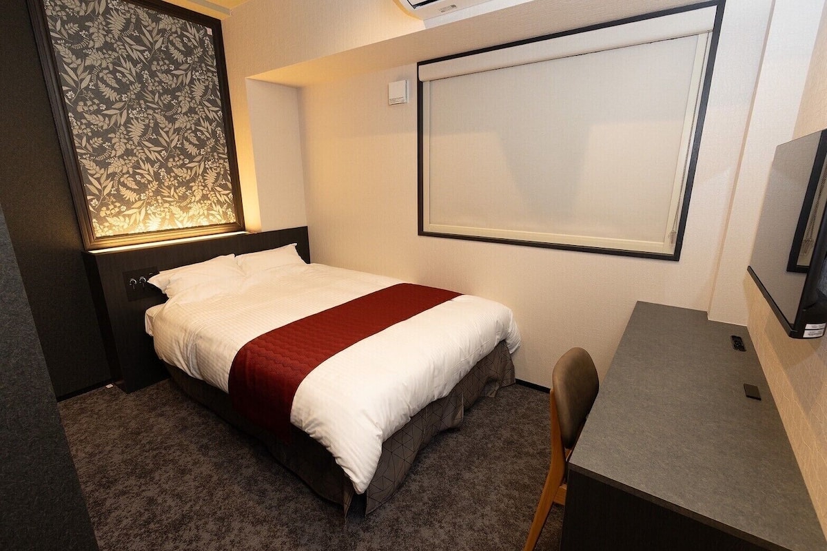 Una habitación de hotel con cama, escritorio, silla, televisor y ventana.