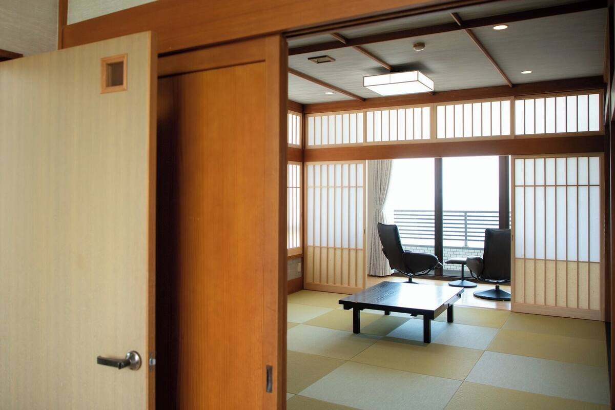 A traditional Japanese room with tatami flooring, a tatami mat table, a black chair, and a sliding shoji screen.