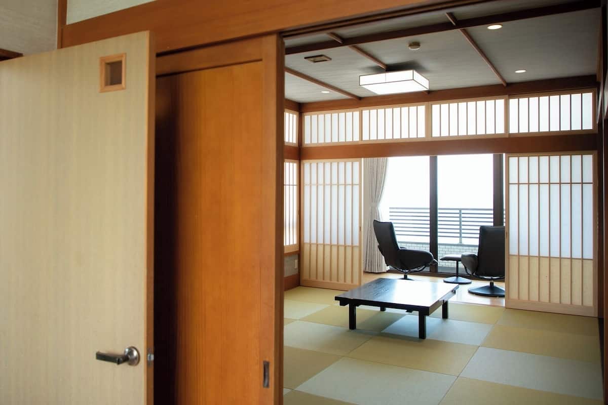 Une pièce de style japonais traditionnel, avec un sol recouvert de tatamis, une table en tatami, une chaise noire et un paravent coulissant de type shoji.
